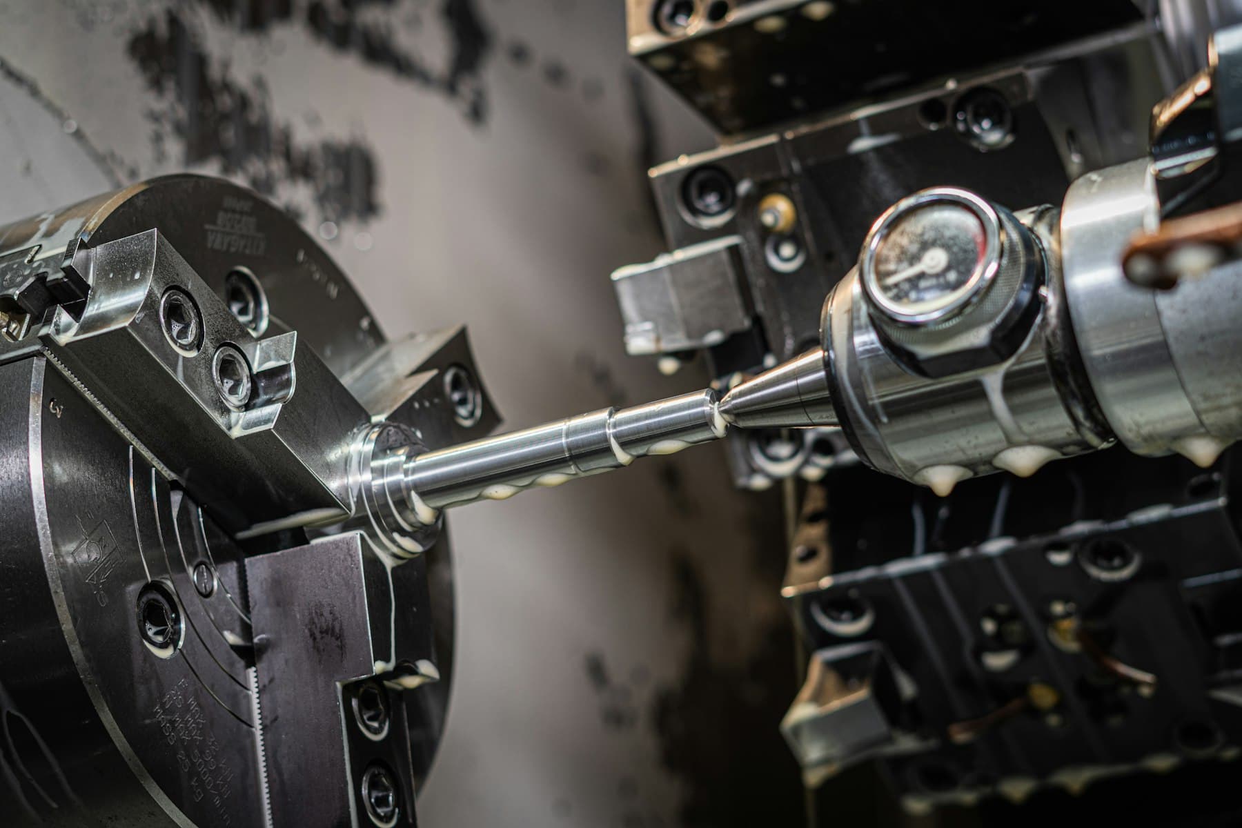 Close view of a CNC lathe cutting a steel shaft held in a three-jaw chuck.